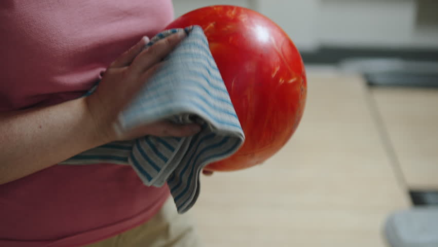 Young woman wipes bowling ball with microfiber cloth, close-up. Removing oil from ball surface, increasing friction control on bowling equipment.