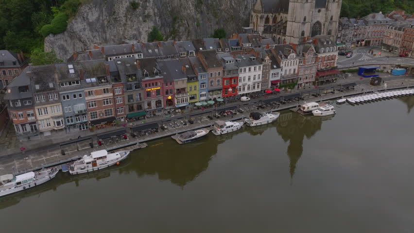 Colorful buildings along the Meuse river with the Collegiate Church of Our Lady at dusk in Dinant, Belgium. Boats moor along the river bank
