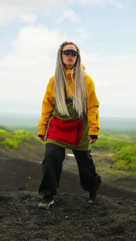 A Young Woman in Vibrant Athletic Wear Standing Confidently on a Volcanic Landscape, Showcasing Contemporary Outdoor Fashion Against a Dramatic Sky Backdrop