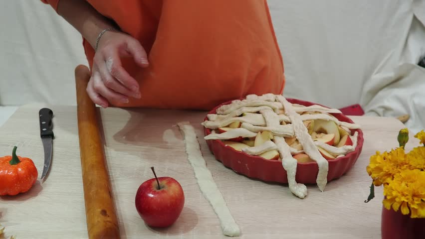 A girl is making apple pie at home. Autumn fall baking background with pumpkins, apples, nuts, food ingredients and seasonal spices. Cooking pumpkin or apple pie for Thanksgiving and autumn holidays, 