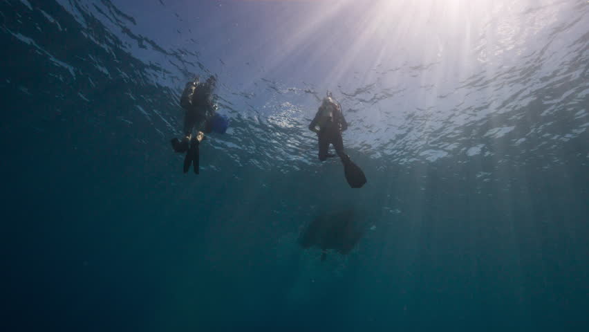 Underwater shot looking up towards two SCUBA Divers and a small Rigid Inflatable boat approaching them