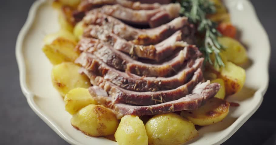 freshly baked pork neck tenderloin and baked potatoes on big white plate, food closeup
