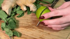 Cutting Fresh Lime in Half with Kitchen Knife A girl holds a lime in her hand and squeezes out the juice against the background of ginger and mint on a wooden board - Powered by Shutterstock - Get 15% off with code: PIKWIZARD15