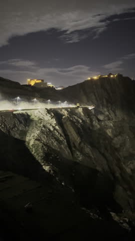 Stunning overhead shot of a brilliantly lit, serpentine mountain switchback road snaking through the pitch black landscape at high elevation in Saudi Arabia.