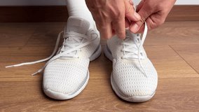Close up of a woman tying shoelaces on white sneakers indoors. Sport shoes on wooden floor. Preparing for workout, fitness, jogging, training or daily casual activity. - Powered by Shutterstock - Get 15% off with code: PIKWIZARD15