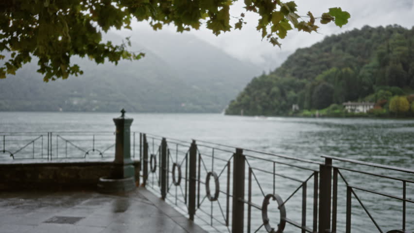 Blurred lakeside walkway with metal railing and distant hills in soft bokeh outdoor; background backdrop copyspace calm.