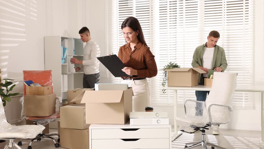 Moving day. Workers packing different belongings and woman with clipboard in office