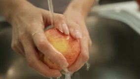 Close-up of hands washing a red apple under tap water, in a kitchen.. Ideal for health, hygiene. - Powered by Shutterstock - Get 15% off with code: PIKWIZARD15