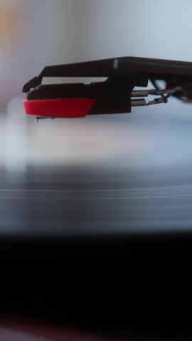 Macro shot of a turntable stylus playing a spinning vinyl record, symbolizing retro music, nostalgia, and analog sound quality. vertical video