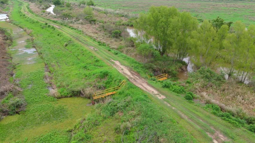 Aerial orbit at rural dirt road along green trees and small bridge over canal in Paraná Delta, Argentina.