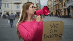 Young woman holds pink megaphone to mouth and displays cardboard sign on street; solidarity activism. - Powered by Shutterstock - Get 15% off with code: PIKWIZARD15