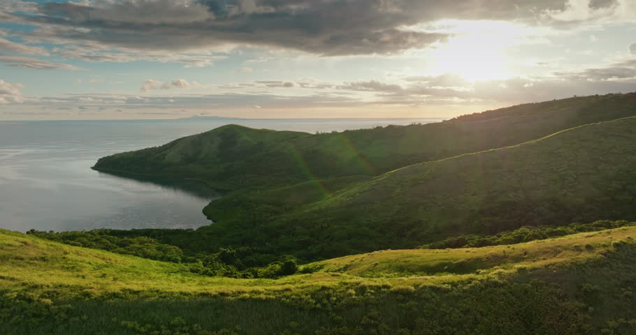 Fiji landscape at sunset featuring lush green rolling hills meeting the calm ocean bay under a vibrant sky, creating a serene and picturesque tropical scene