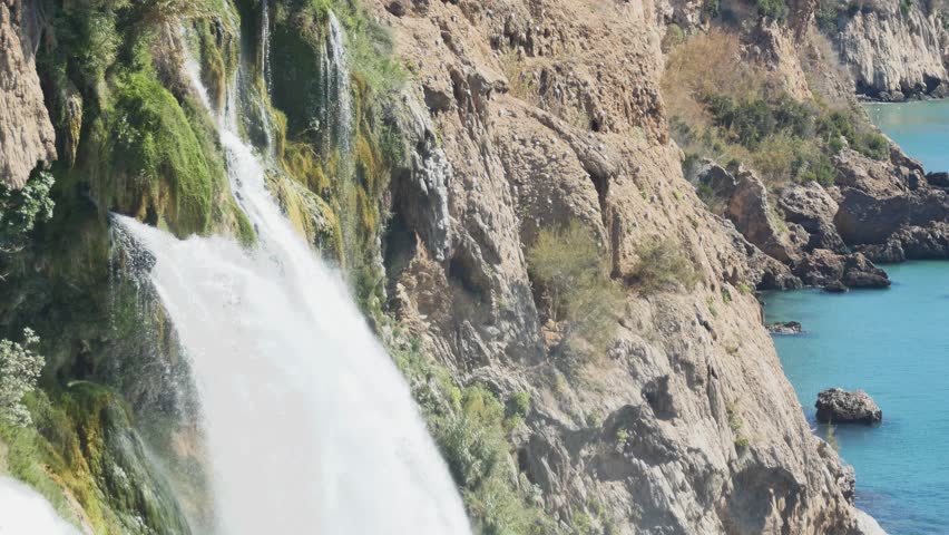 A detailed view of the Lower Düden Falls, showcasing the geological layers and the vibrant green moss and vegetation clinging to the towering brown cliffs.