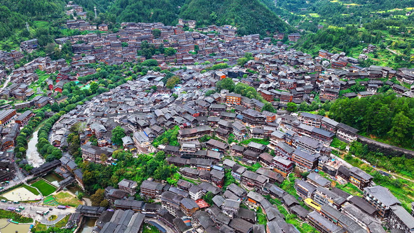 Qianhu Miao Village in Xijiang, Guizhou. Aerial shot of a spectacular ancient ethnic minority village with traditional wooden houses nestled in a lush green mountain valley in China.