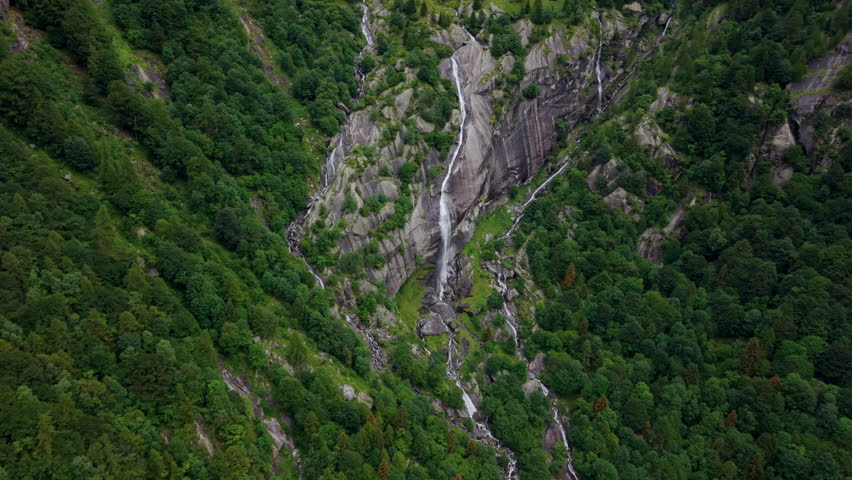 Aerial drone shot in full top-down view rising and pulling back over a waterfall surrounded by rocks and vegetation in the Swiss Alps.