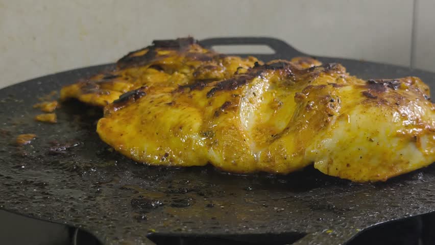 Chicken meat, marinated with spices, is grilled on a flat, non-stick pan. The spices sizzle, releasing a delicious aroma. Close-up shot shows the chicken browning perfectly on the grill.
