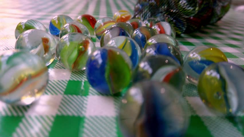 Closeup dolly of colorful striped glass marble balls spread on checkered table from net bag