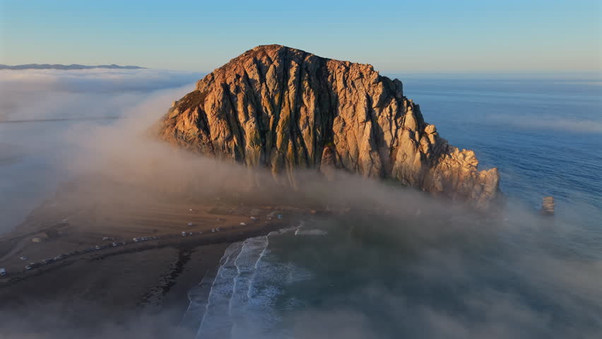Stunning aerial footage of a majestic Morro rock formation shrouded in mist next to the vast ocean, perfect for nature projects, presentations, and educational content. Morro Bay, California, USA
