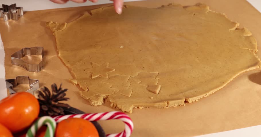 A person uses cookie cutters to make gingerbread cookies from rolled dough. It