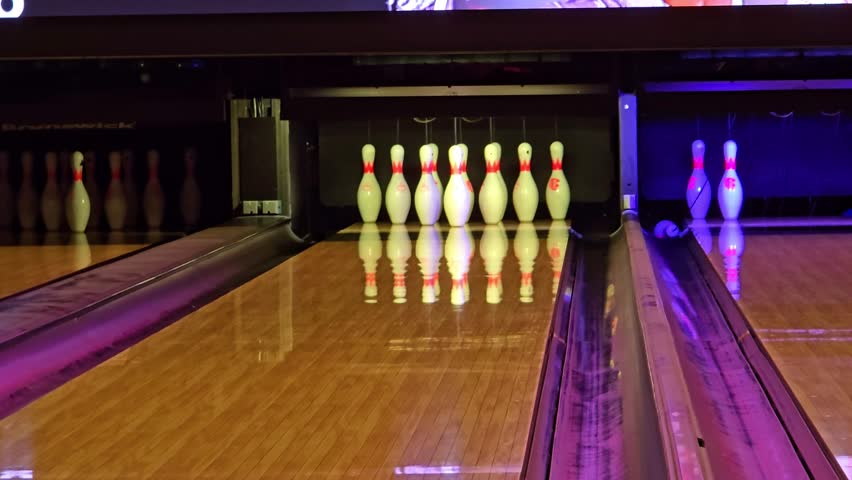 Fixed shot of bowling pins as the ball rolls down the lane and falls into the gutter.