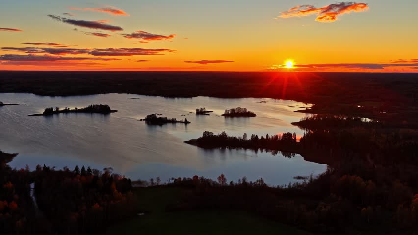 Aerial drone view at golden hour showing glowing red and orange sunset over forest and lake horizon