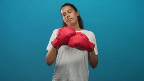 Woman in white t-shirt wearing red boxing gloves raises both arms in a shrug gesture against a blue studio backdrop; nonchalance. - Powered by Shutterstock - Get 15% off with code: PIKWIZARD15