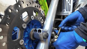 Mechanic wearing blue nitrile gloves installing or adjusting the front axle and brake components on motorcycle. Disc brake rotor, axle mount, and detailed mechanical parts in workshop setting - Powered by Shutterstock - Get 15% off with code: PIKWIZARD15