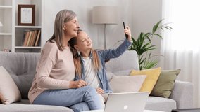 Grandmother senior lady and blonde little granddaughter taking selfie on phone sitting on sofa, looking at photos hugging. - Powered by Shutterstock - Get 15% off with code: PIKWIZARD15