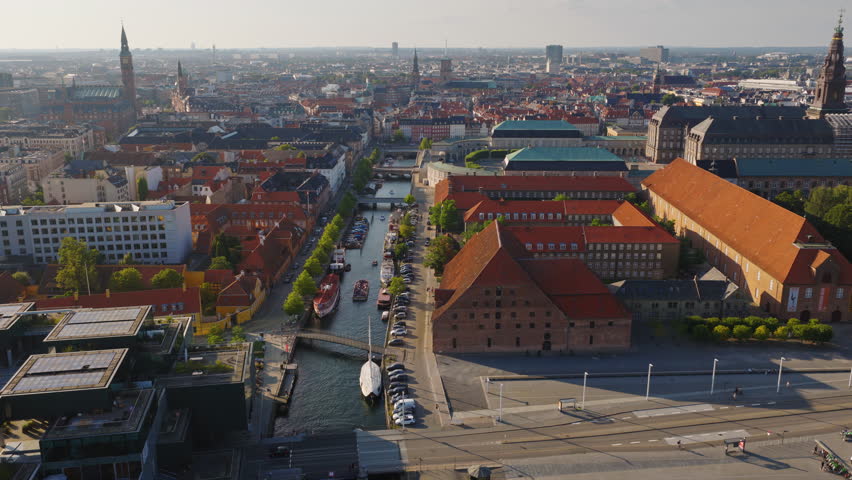 Aerial drone view of Christianshavn canal with red-roofed historic buildings and docked boats in central Copenhagen, Denmark