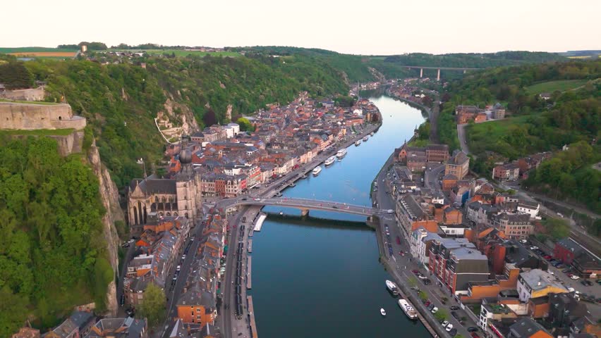 citadel church meuse river below mountains above traffic bridge boats evening time green fields beyond dinant revealing left pull pullback top shot belgium