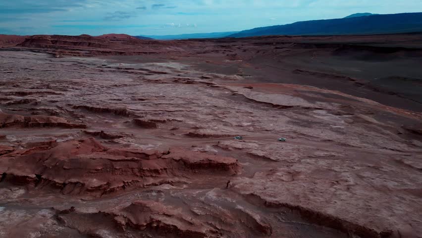 Sideways tracking drone aerial following cars through Valle de la Luna, San Pedro de Atacama, Chile with Mars-like red desert landscape