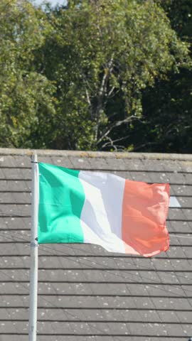 Irish flag flutters on rooftop flagpole, bright daylight, residential area, gentle summer wind, Edinburgh