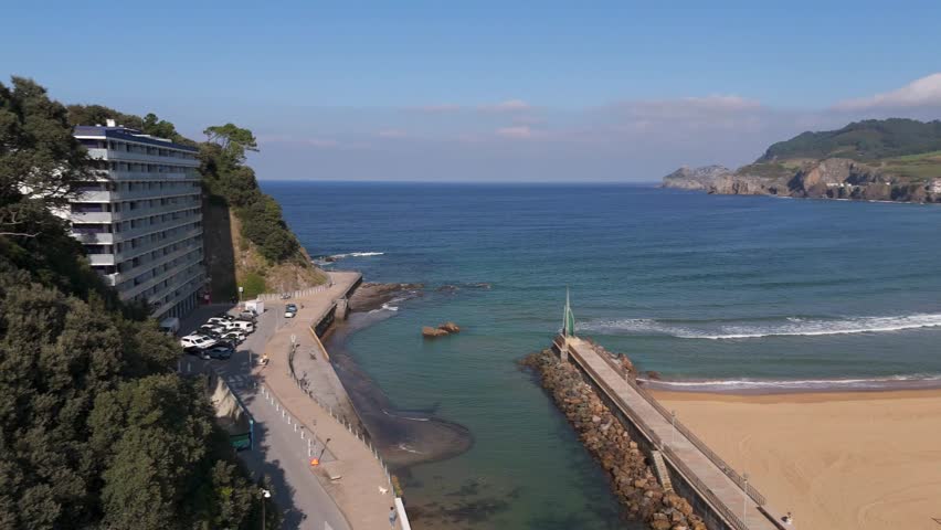 A Stone pier walkway extending toward the blue sea bordered by sandy beach and rocky shorelines