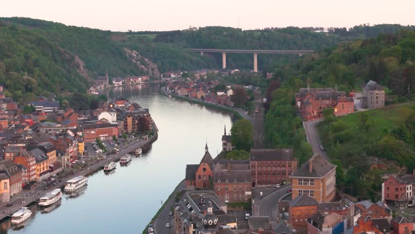 meuse river boat sailing town both sides road traffic highway bridge green cover vibrant landscape dinant to left right far side panning belgium aerial riverside