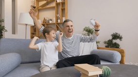 Young father playing video game with wireless joystick while son sits beside supporting him, both smiling and giving high five after victory - Powered by Shutterstock - Get 15% off with code: PIKWIZARD15