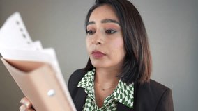 A close-up headshot of tired fatigue young Indian businesswoman holding folder of documents against a gray background - Powered by Shutterstock - Get 15% off with code: PIKWIZARD15