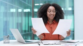 Joyful young African American businesswoman is satisfied with results of a financial report she is reviewing while sitting at a workplace in office. Female manager is happy with positive indicators - Powered by Shutterstock - Get 15% off with code: PIKWIZARD15