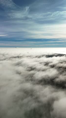 A drone vertical view of a forested hilly landscape in autumn shrouded in fog under blue, white sky with shining sun in the Czech Republic