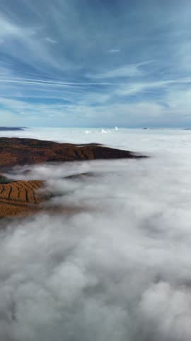 A drone vertical shot of a hilly autumn forested landscape shrouded in fog under blue, white sky in the Czech Republic