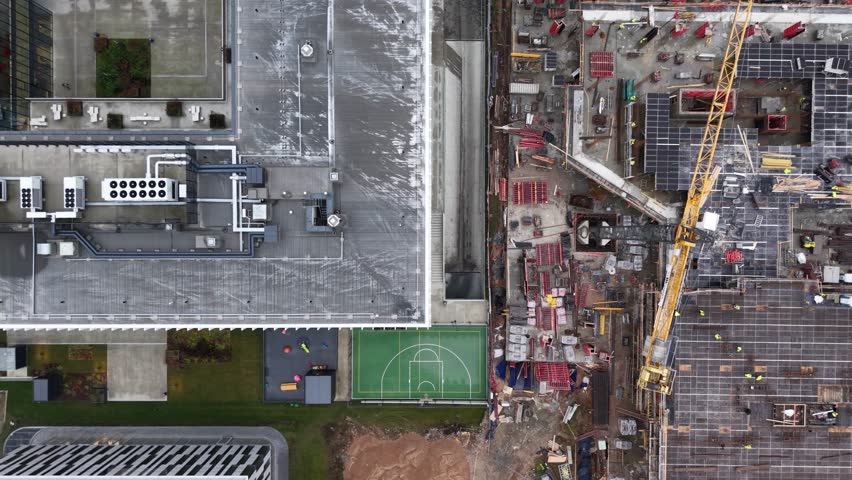High-angle drone image showing a large-scale construction site with workers, scaffolding, rebar, formwork, and materials during the concrete framework phase of a multi-story building.
