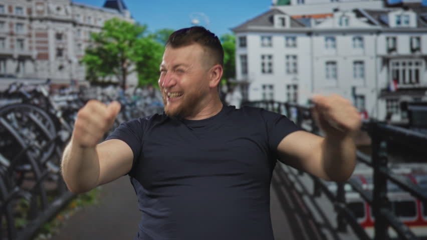 Man smiling and raising clenched fists with visible forearms on a city street in amsterdam; victory joy celebration.