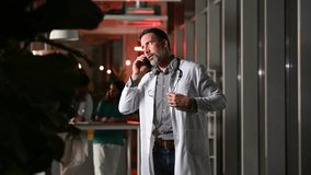 Mature male doctor having a serious and stressful phone conversation in a modern hospital at night. His colleagues are working in the background - Powered by Shutterstock - Get 15% off with code: PIKWIZARD15
