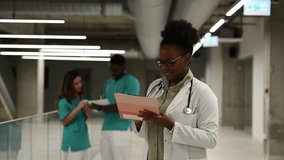 Portrait of a young african american female doctor holding a clipboard in a modern hospital hallway, smiling confidently at the camera - Powered by Shutterstock - Get 15% off with code: PIKWIZARD15