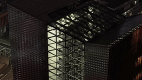 Nighttime view through a geometric glass wall showing a lit interior lobby with contemporary decor, reflective flooring, and structured lighting in a commercial or office building. - Powered by Shutterstock - Get 15% off with code: PIKWIZARD15