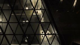 Nighttime view through a geometric glass wall showing a lit interior lobby with contemporary decor, reflective flooring, and structured lighting in a commercial or office building. - Powered by Shutterstock - Get 15% off with code: PIKWIZARD15