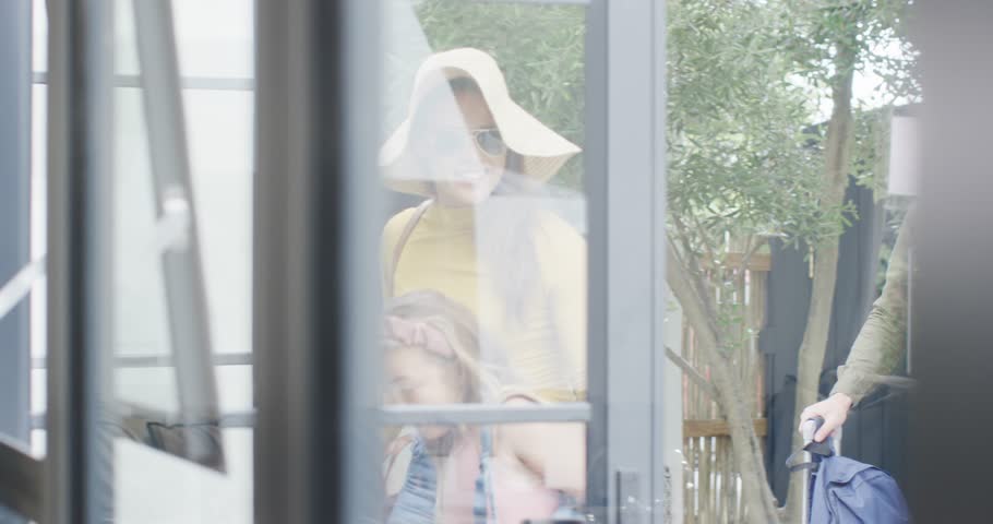 Diverse family walking through door into room, carrying rolling bag, hugging and pointing joyfully. Family, togetherness, relaxation, modern, candid, candidness, warmth