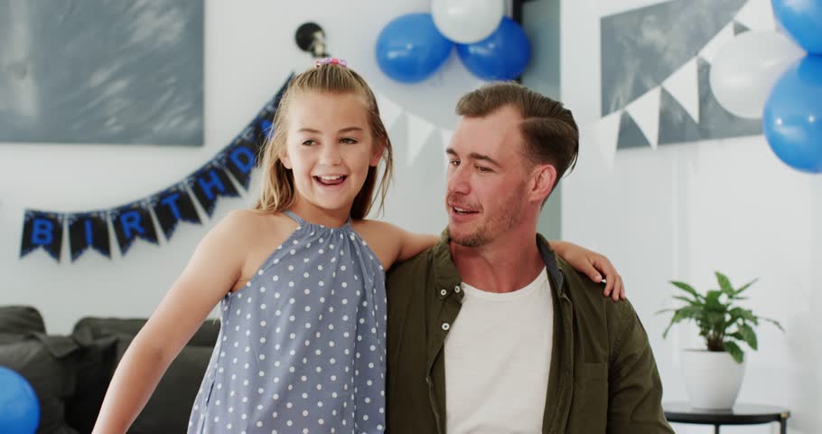 Diverse family watching mother bringing birthday cake at home father blowing candles, girl hugging. Family, celebration, joy, togetherness, warmth, affection, happiness