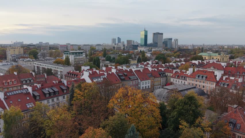 Aerial drone flyover in autumn over the Old Town of Warsaw, Poland, showing golden trees, colorful rooftops, and a beautiful view of the Vistula River under warm sunlight.