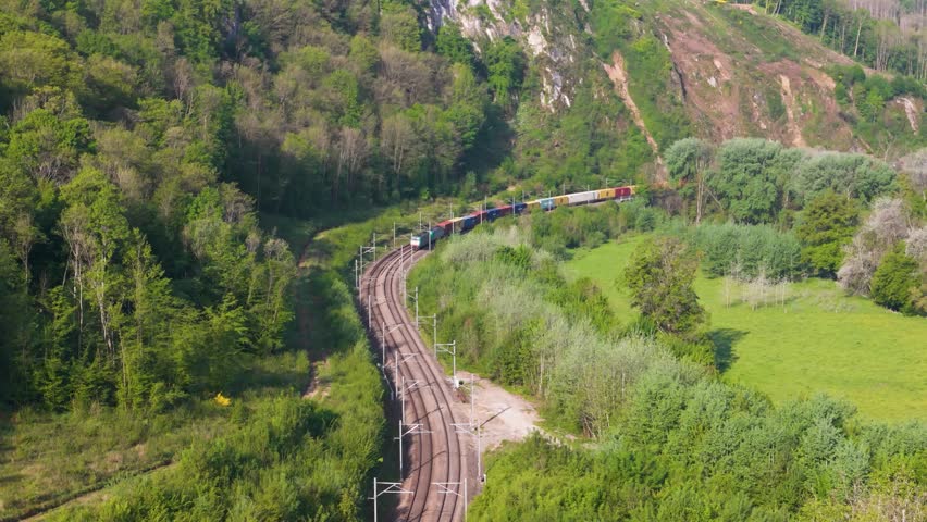 freight train running tracks surrounded by thick jungle green covered hills both sides overhead aerial shot railway transportation dense forest