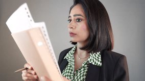 A concerned South Asian woman in a blazer holds a file and pen, reading then looking directly at the viewer with shocked surprised face - Powered by Shutterstock - Get 15% off with code: PIKWIZARD15